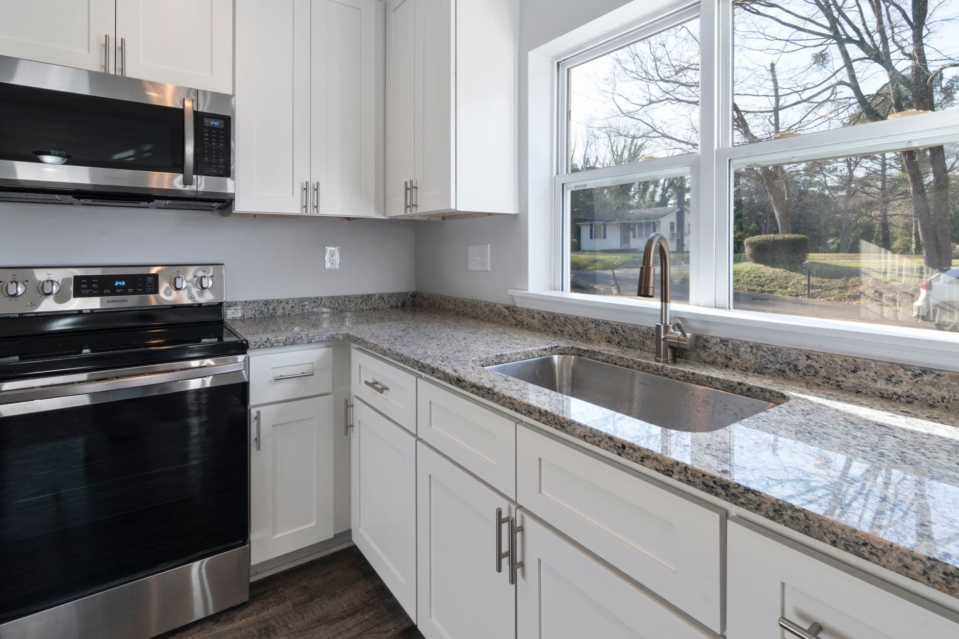 Bright kitchen showcasing granite countertops, stainless steel appliances, and large windows.